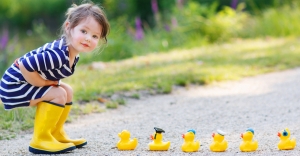 Adorable little girl of 2 playing with yellow rubber ducks in summer park